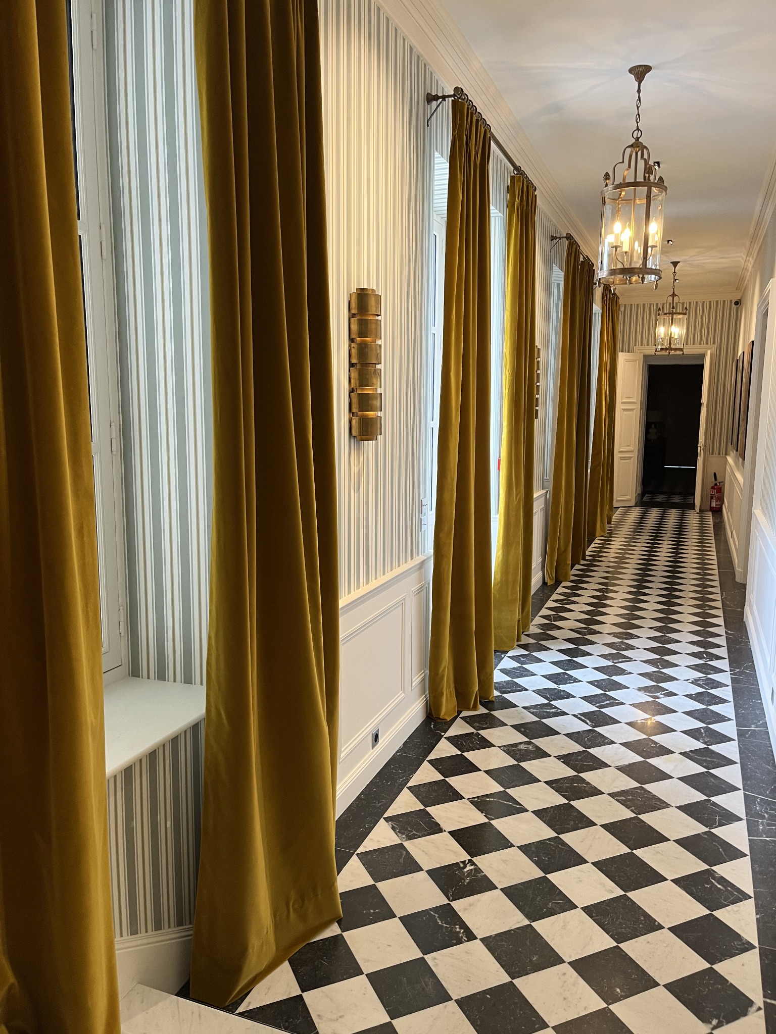 Rideaux ocre dans un couloir aux sols en damier